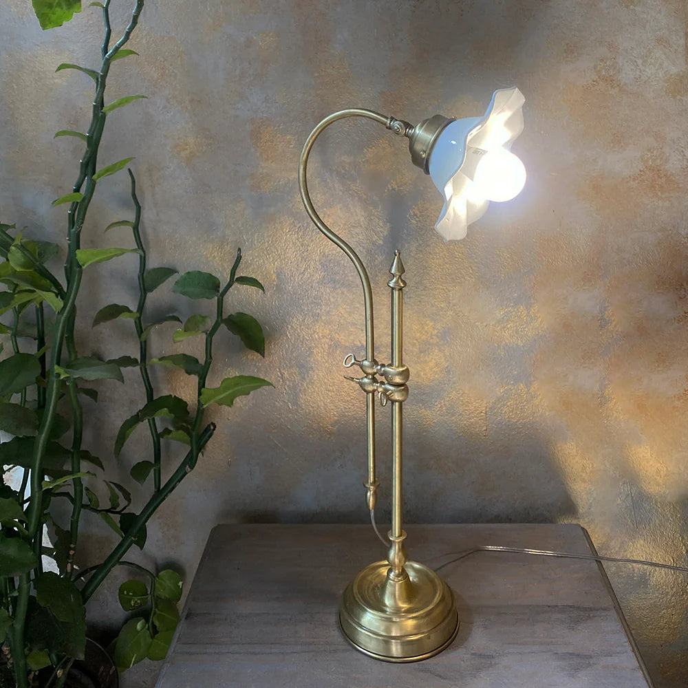 Vintage-style brass desk lamp with a lit bulb on a wooden surface against a textured wall.
