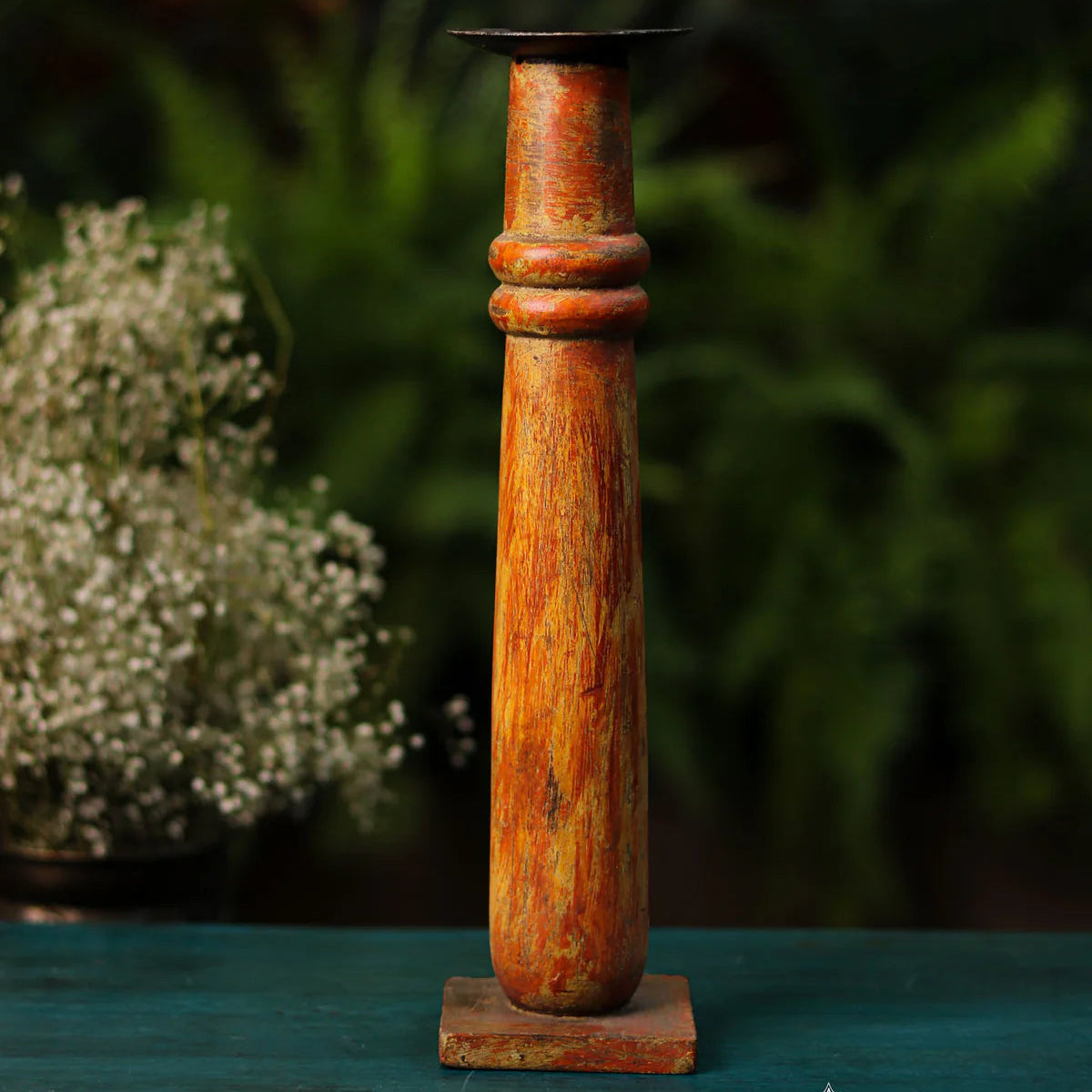 Decorative wooden candle holder on a green surface with blurred greenery in the background