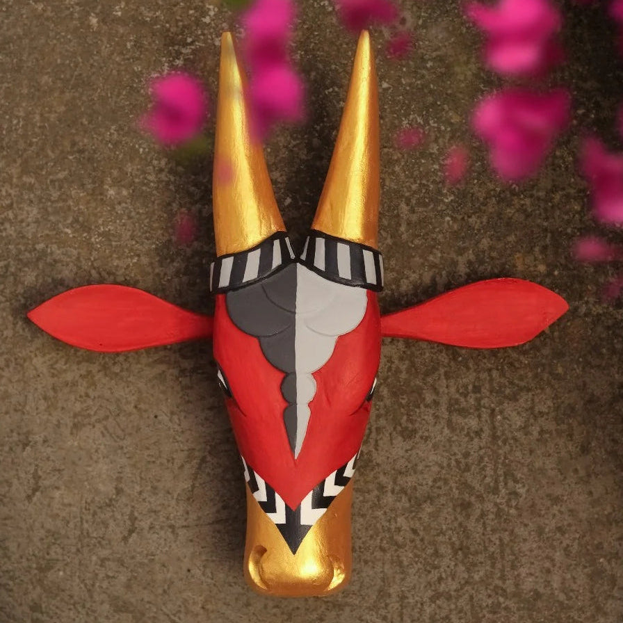 Decorative cow head sculpture with red and gold colors on a brown background with pink flowers.
