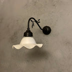 Wall-mounted light fixture with white glass shade and black metal arm on a textured wall.