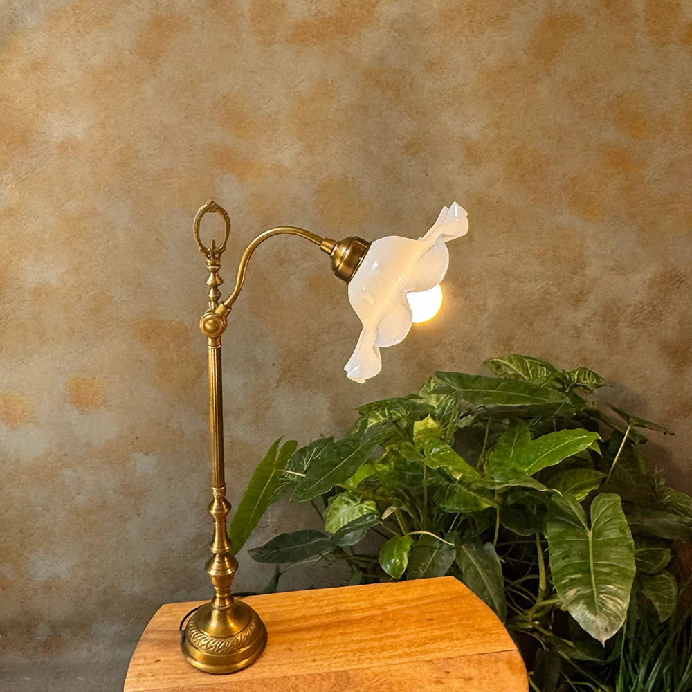 Vintage-style brass lamp with white floral shade on a wooden surface against a textured wall.