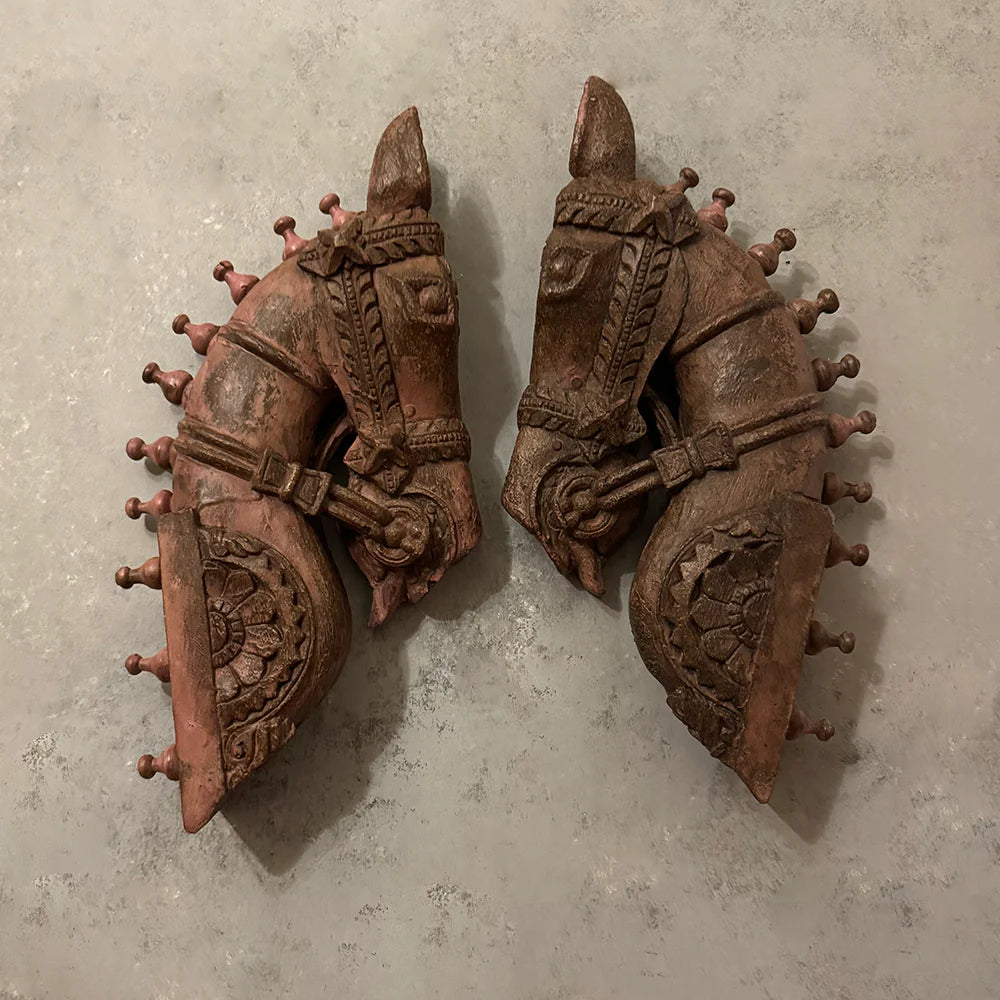 Two ornate wooden horse head sculptures on a textured gray background