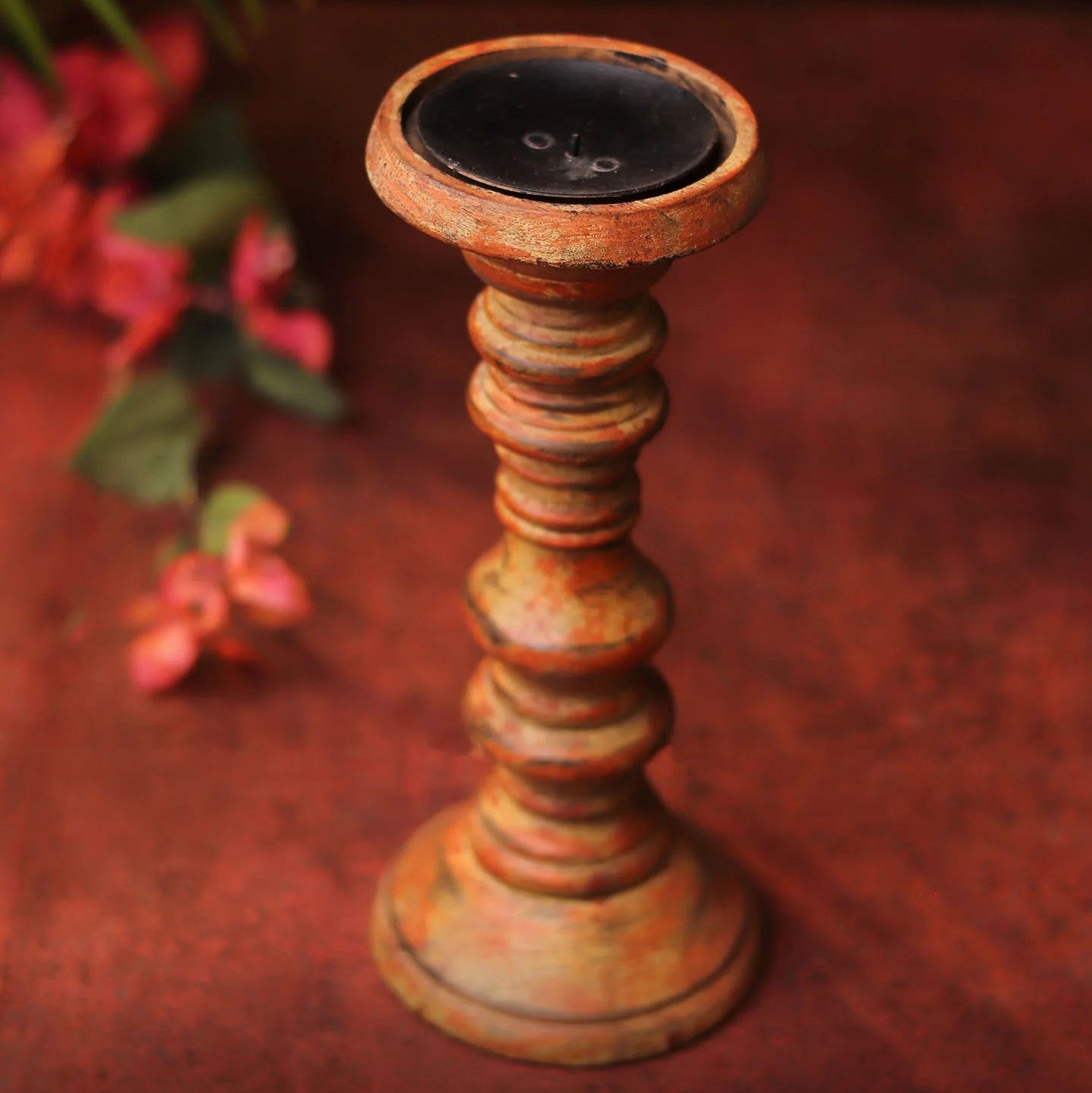 Wooden candle holder on a textured surface with blurred flowers in the background