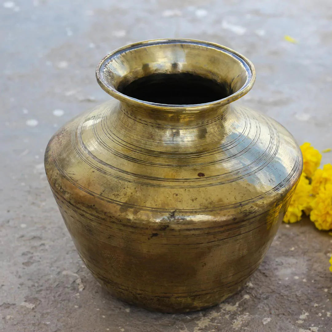 Brass pot on a concrete surface with yellow flowers
