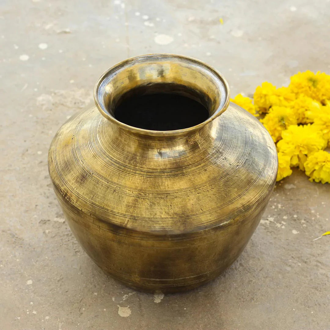 Brass pot with dark liquid on a light gray surface with yellow flowers.