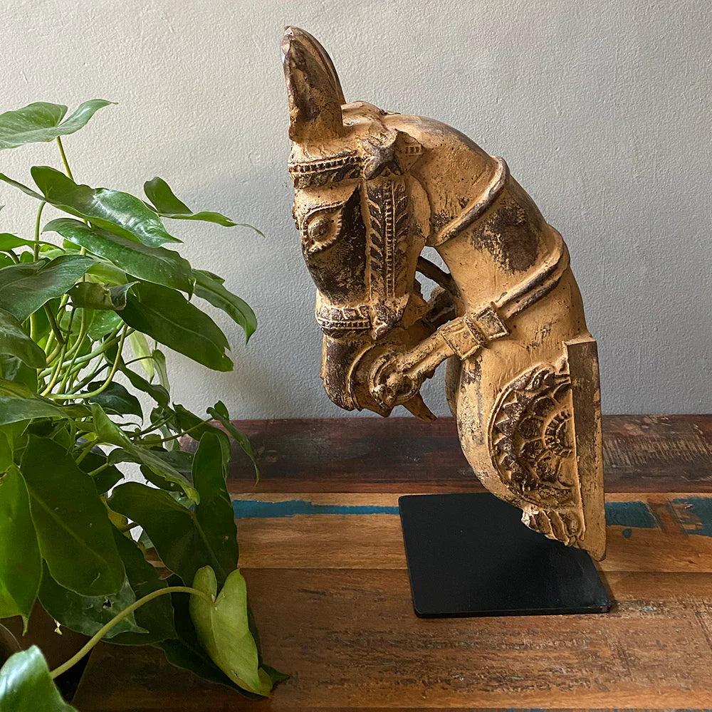 Decorative horse head sculpture on a wooden surface with a plant in the foreground.