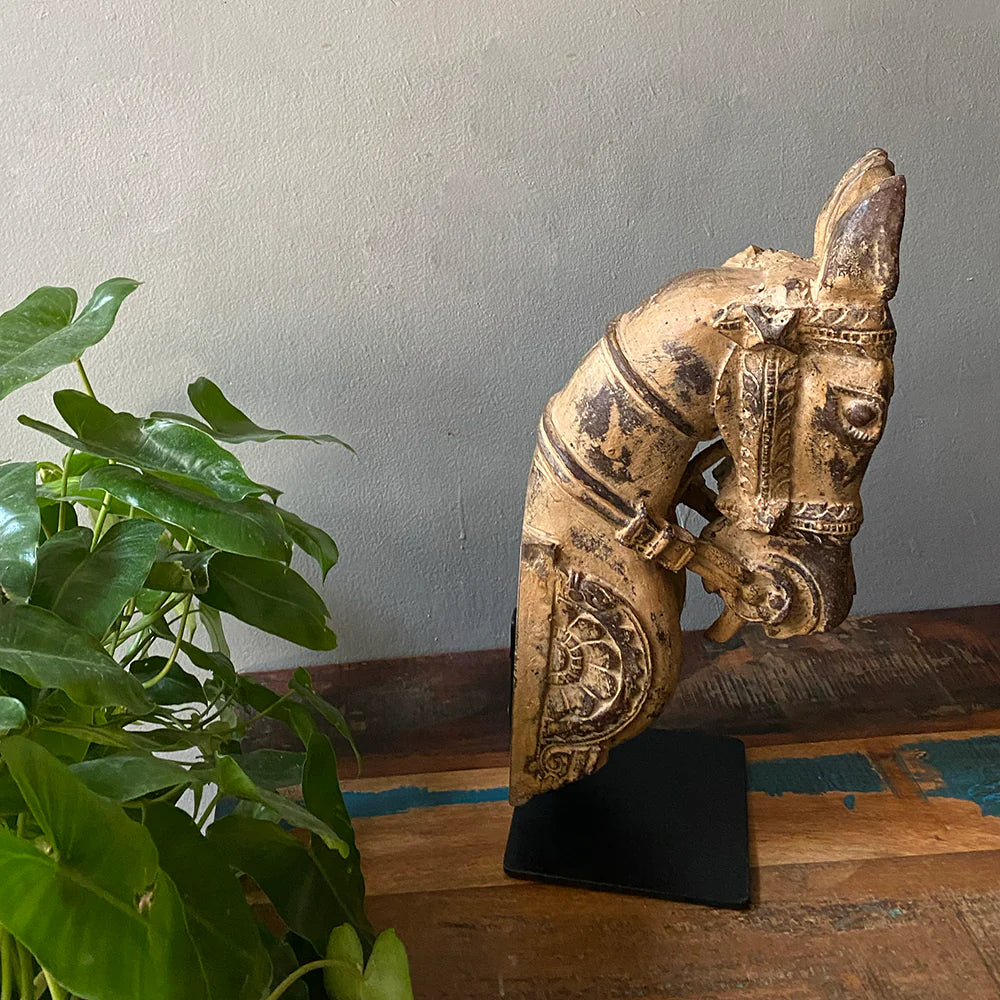 Decorative horse head sculpture on a stand with a plant in the foreground