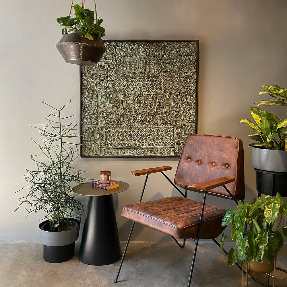 Brown leather chair in a room with plants and a decorative wall piece.