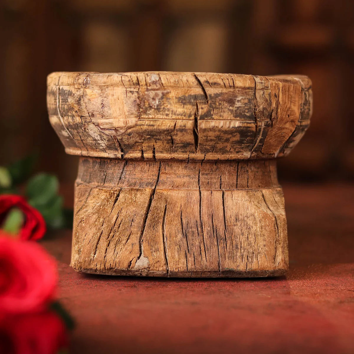 Wooden block with a rustic texture on a dark surface, surrounded by red flowers.