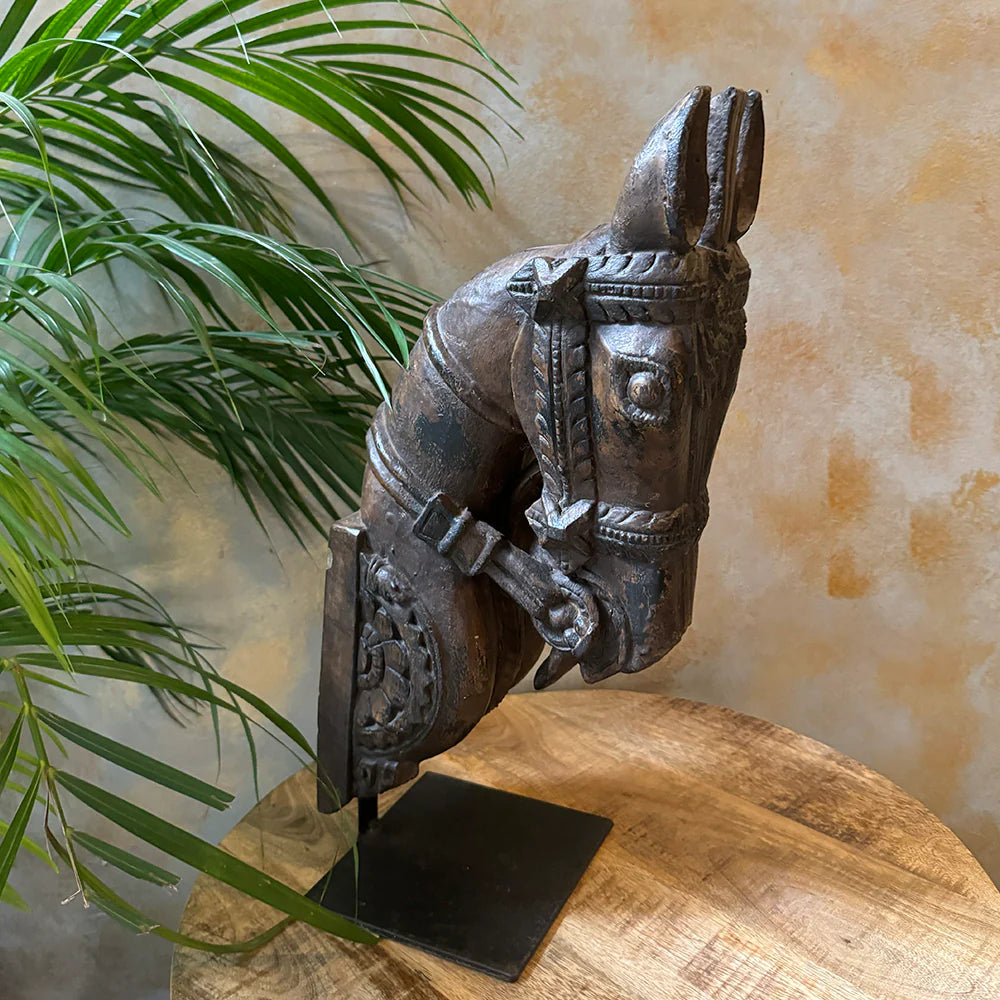 Carved wooden horse head sculpture on a stand with a plant in the background