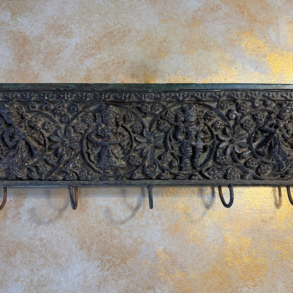 Decorative metal wall hook with intricate designs on a textured wall.