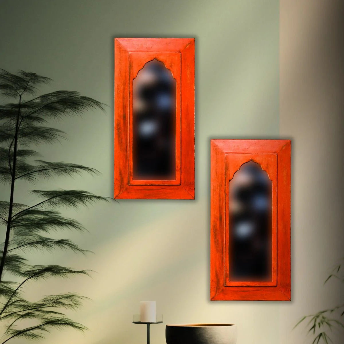 Two red mirrors on a wall with a decorative table and plant in the foreground.