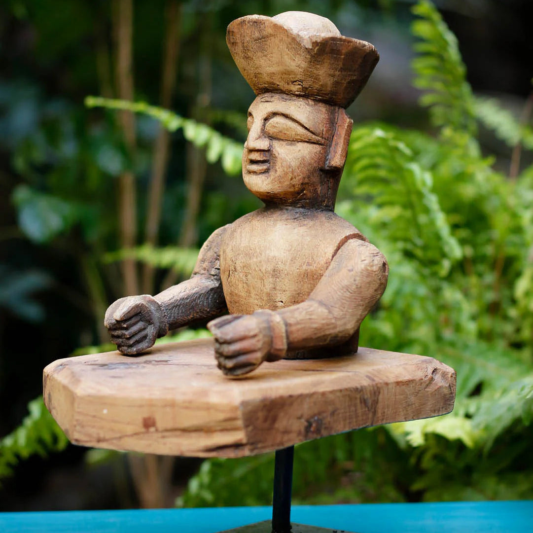 Wooden sculpture of a figure on a stand with a blurred green foliage background