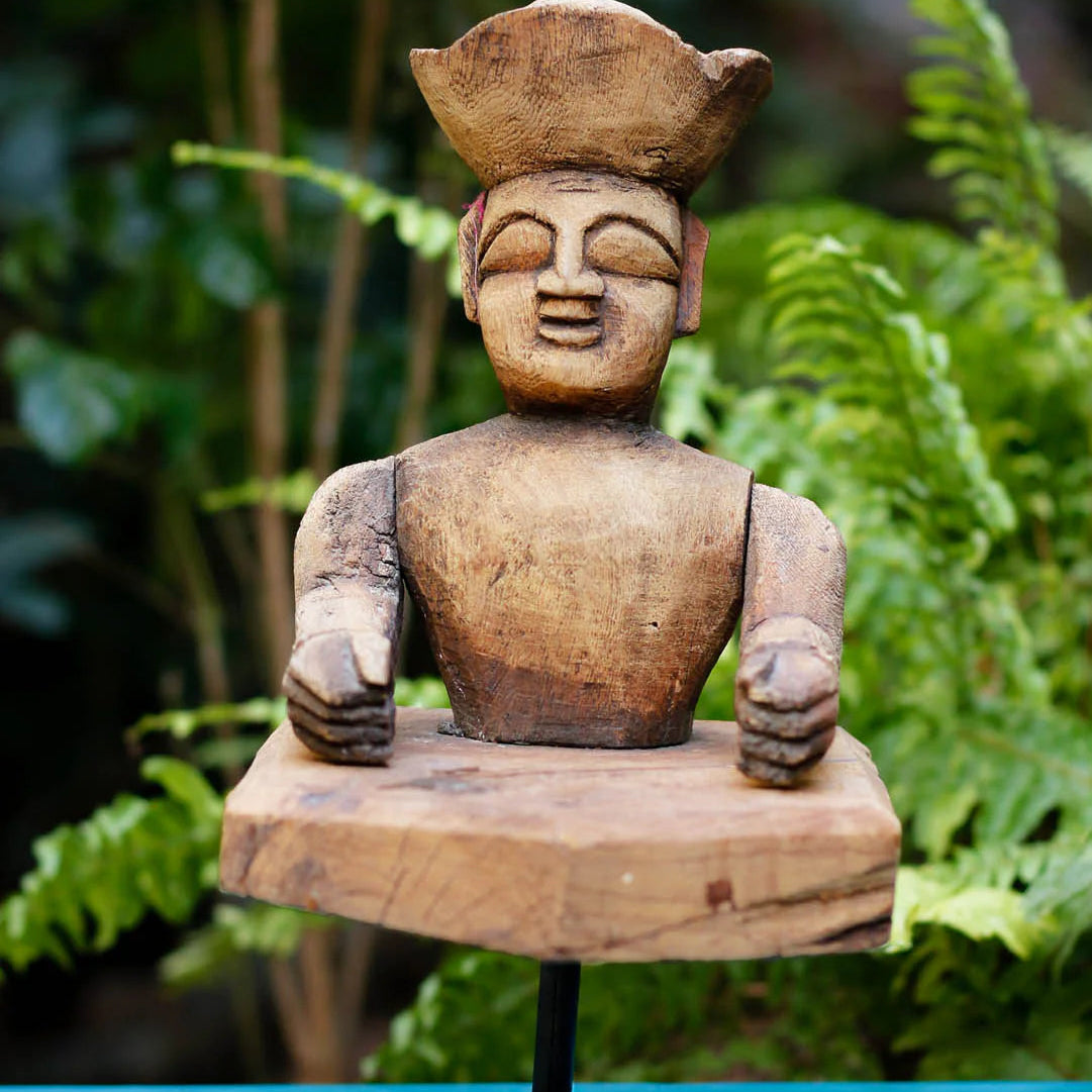 Wooden sculpture of a figure on a stand with a natural background