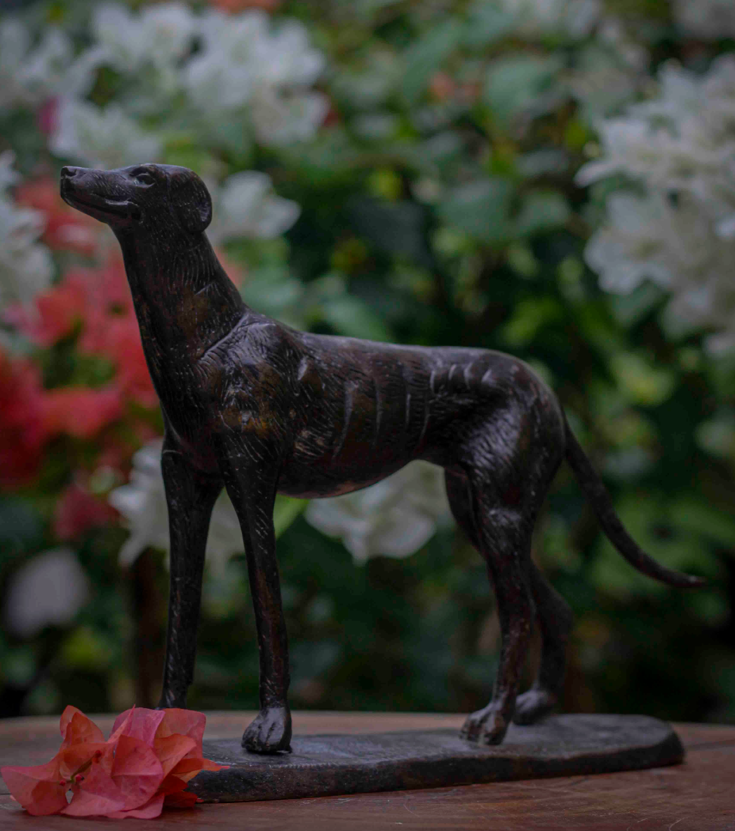 Bronze statue of a dog on a wooden base with a blurred floral background