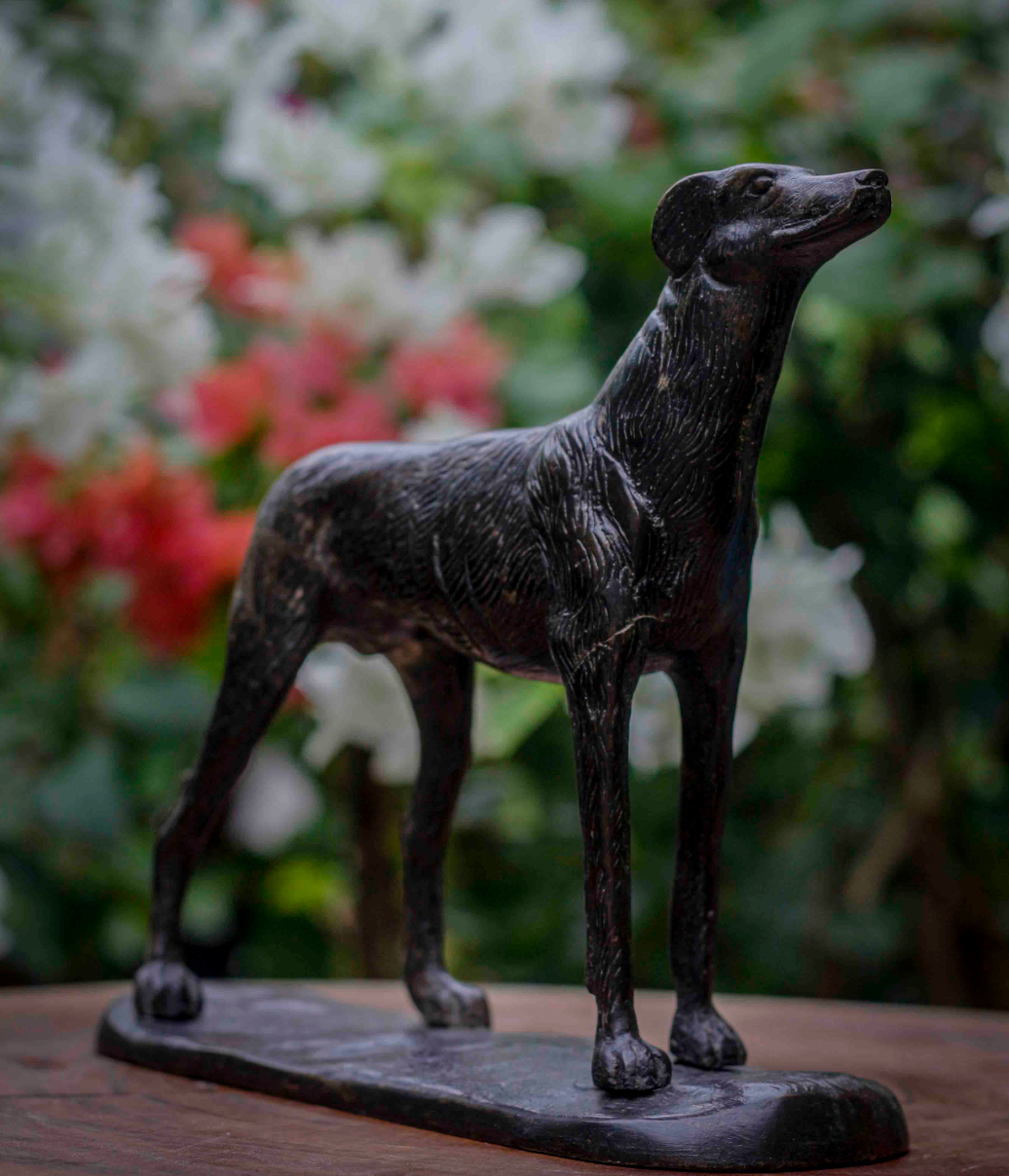 Bronze statue of a dog on a wooden surface with a blurred floral background