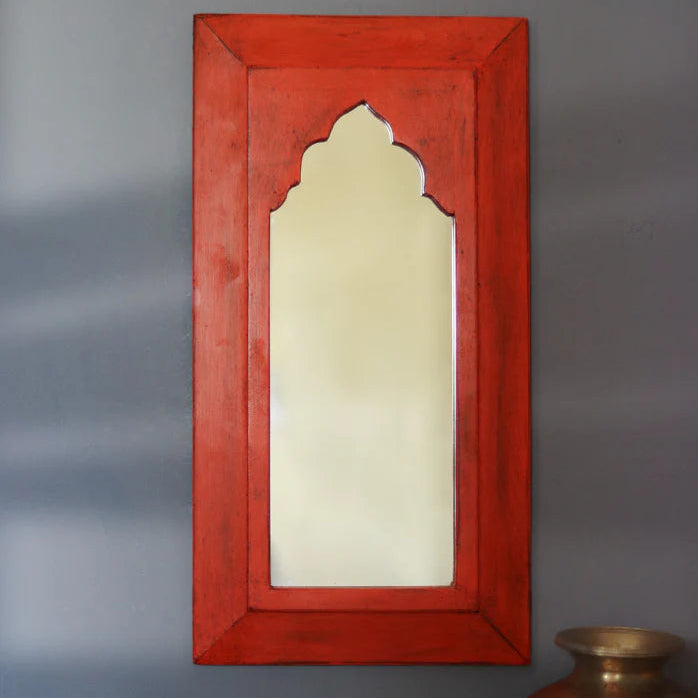 Red framed mirror on a gray wall with a vase and flowers in the foreground.