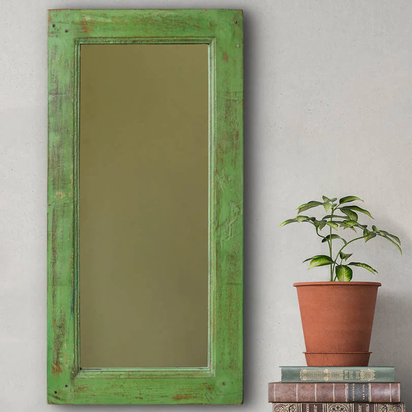 Green-framed mirror on a wooden console with books and a plant