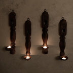 Four wooden candle holders with candles on a textured wall.