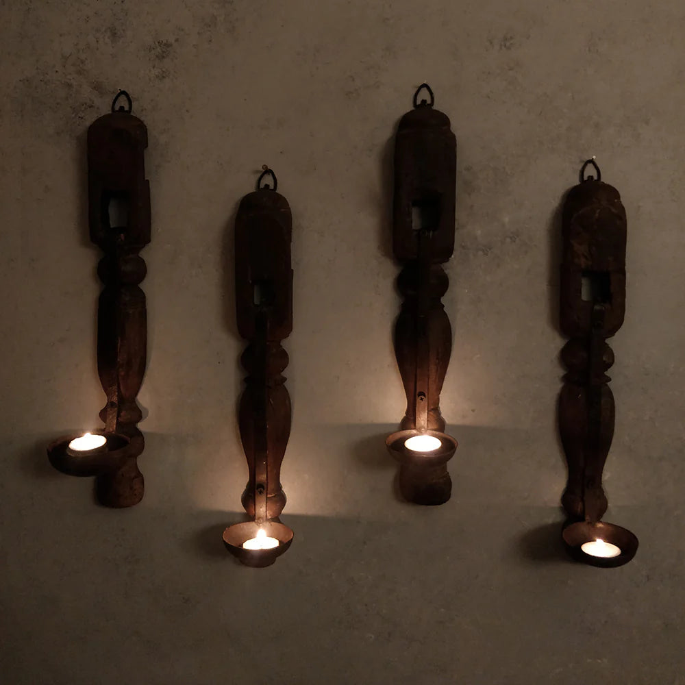 Four wooden candle holders with candles on a textured wall.