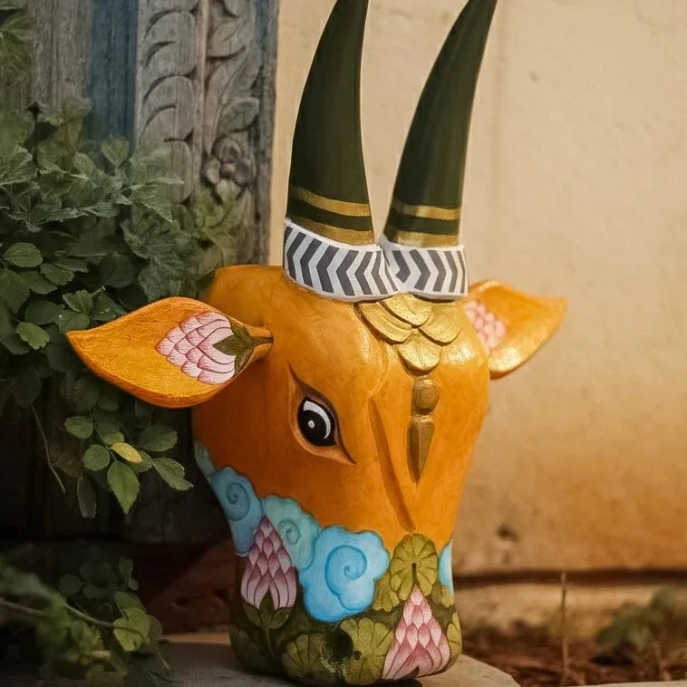 Decorative animal head with painted features and green horns on a neutral background
