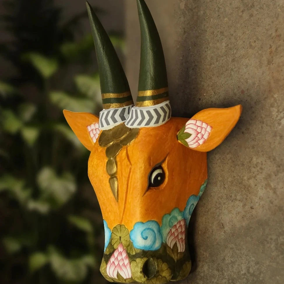 Decorative wall art of a painted animal head with intricate designs on a textured wall.