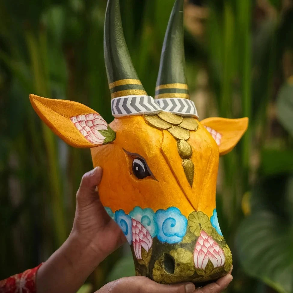 Hand holding a colorful cow head sculpture against a green leafy background