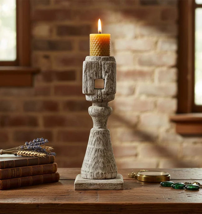Wooden candle holder with a lit candle on a wooden surface against a brick wall.