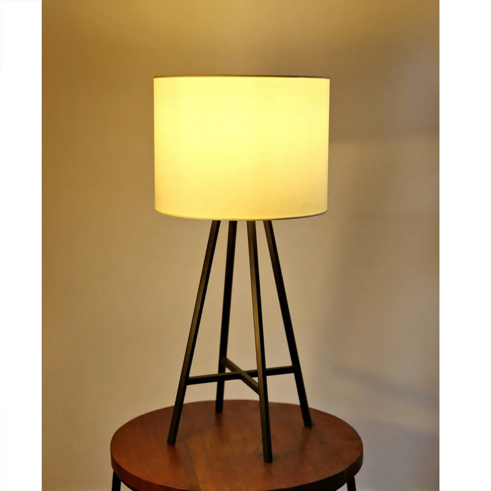 Floor lamp with a round wooden base and tripod metal stand against a plain wall.